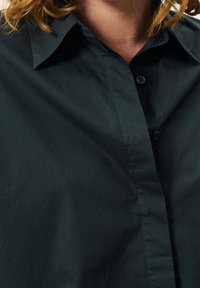 Camicia nera con bottoni, caratterizzata da un colletto classico, una texture liscia e una pattina dei bottoni nascosta per un look pulito.