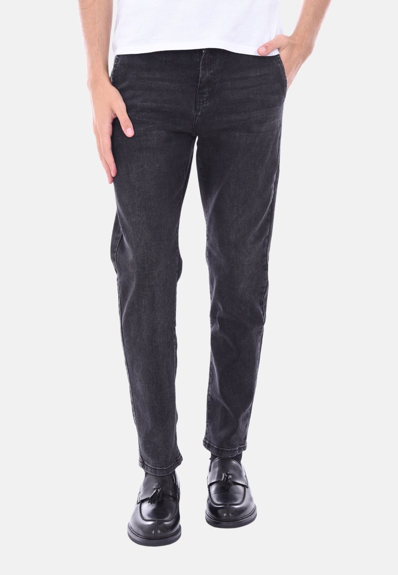 Jeans in denim nero con vestibilità slim, caratterizzati da tasche frontali e una leggera texture consumata, abbinati a scarpe in pelle nere.