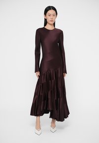 Dolga bordo satenasta obleka z dolgimi rokavi, asimetrično zasnovo in plasteh volanov na spodnjem robu. Oblečena s belimi čevlji z ostrim vrhom.