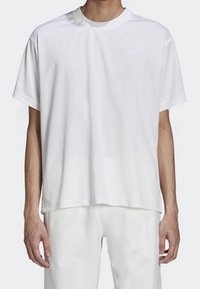 Bílý krátký rukáv tričko vyrobené z jemné tkaniny, s kulatým výstřihem, uvolněným střihem a jemným texturovaným vzorem. V kombinaci s světlými kalhotami.