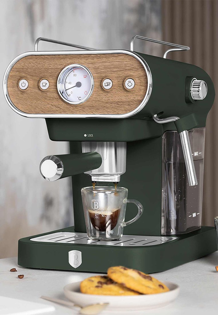 Tmavě zelený espresso kávovar se dřevěnými akcenty, kulatým měřičem, chromovanými detaily a skleněnou šálkem naplněným espressem pod výtokem.