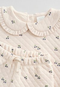 Completo per neonati in cotone rosa chiaro trapuntato, con colletto arricciato e motivo a bacche in blu scuro e verde sparse su cima e pantaloni.