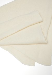Zacht, licht crèmekleurig gebreid dekentje, gevouwen. Heeft een gladde textuur en gelijkmatige stiksels, met een eenvoudig ontwerp en geen zichtbare patronen.