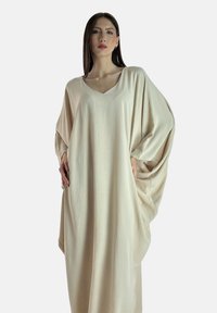 Beige oversized jurk gemaakt van textuurstof; heeft een V-hals en brede mouwen, die losjes tot de enkels hangen.