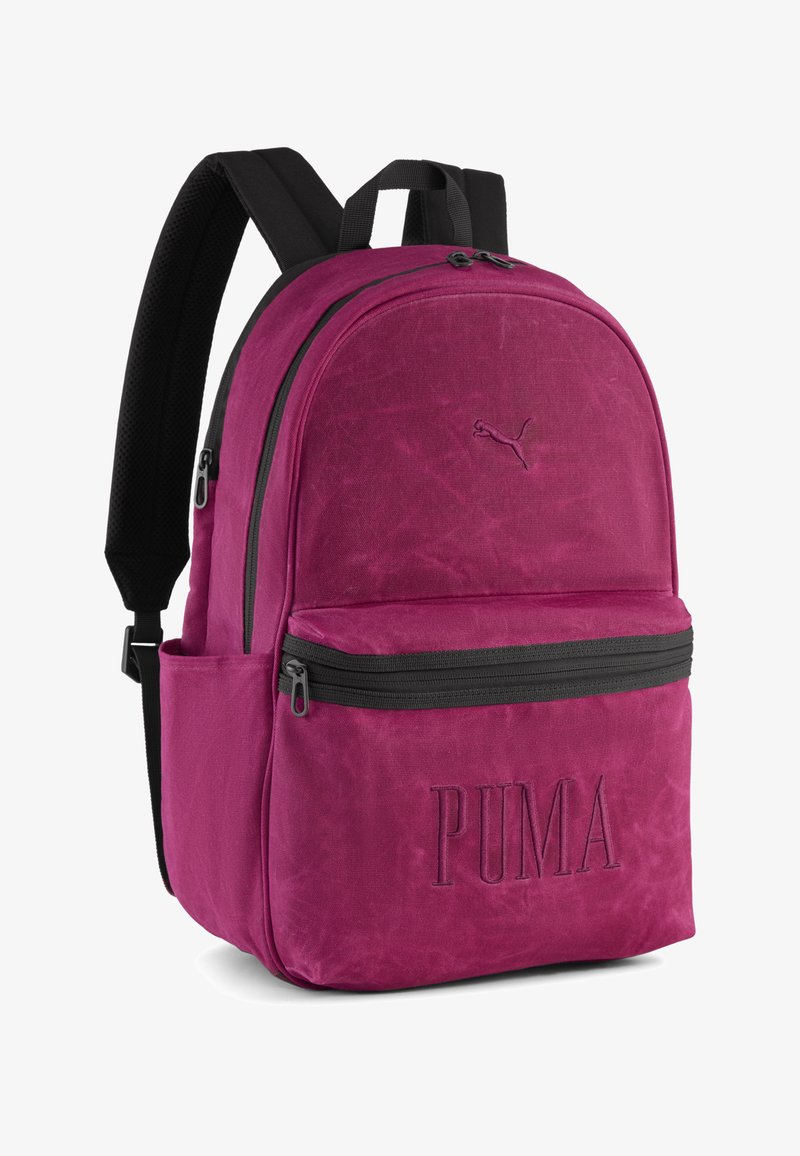 Zaino in tessuto magenta con una texture liscia, un ampio scomparto principale, tasca frontale con zip, dettagli neri e logo "PUMA" in rilievo.
