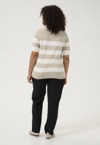 Beige en witte gestreepte trui met korte mouwen en een ronde zoom, gedragen met zwarte broeken en lichtbeige schoenen. Gemaakt van een textuurgebreide stof.