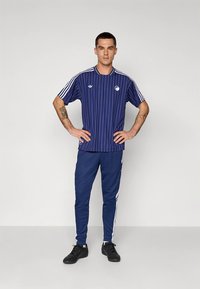 T-shirt atlética às riscas azul-marinho com detalhes em branco, combinada com calças azul-marinho com riscas laterais brancas. Ténis pretos completam o conjunto.