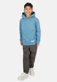 Blå hoodie med känguruficka, ribbade ärmslut och nederkant; tillsammans med grå byxor och vita sneakers med accentremsor.