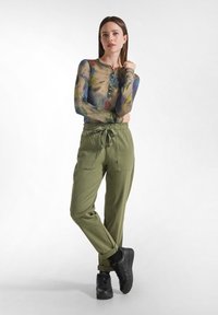 Långärmad, flerfärgad topp med en henley-krage och fem knappar, tillsammans med gröna cargobyxor med dragsko i midjan. Svarta sneakers.