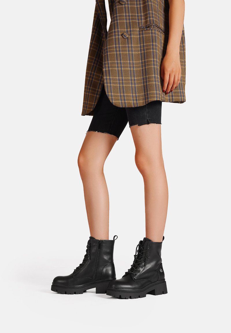 Stivali da combattimento in pelle nera con suola spessa, chiusura con lacci sul davanti e zip laterale. Il design presenta punta rotonda e superficie texturizzata.