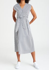 Robe midi rayée en noir et blanc, avec un décolleté en V, des manches courtes, une taille cintrée avec un détail de nœud, et une texture de tissu lisse.