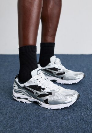 White and silver athletic shoes with mesh and synthetic materials, featuring black accents and a textured sole, worn with black socks.