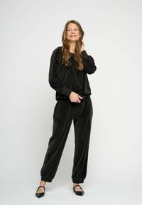 Svart velourträningsoverall med en löst sittande långärmad topp och tapered byxor med elastiska muddar; kombineras med svarta ballerinas.