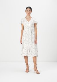 Robe midi florale blanche, avec des manches courtes à volants, un col en V, une taille froncée et un ourlet à volants. Associée à des sandales à brides marron.