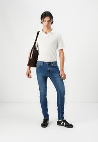 Bijela textured kratka majica, plave slim-fit traperice, crne tenisice s bijelim akcentima i smeša torba za rame.