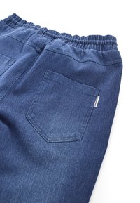 Back view of blue denim pants with elastic waistband and a single square back pocket featuring a small white tag.