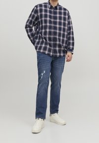 Chemise à manches longues à carreaux bleu marine et blanc, jean en denim clair avec des détails usés, accompagnée de baskets blanches.