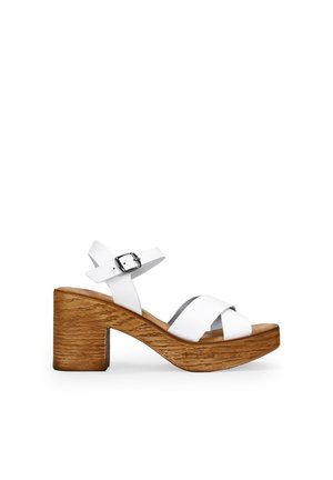 Sandalias de tacón blanco de cuero con tiras cruzadas, cierre de hebilla y un tacón de bloque de madera texturizado. Acabado suave con una suela plana.