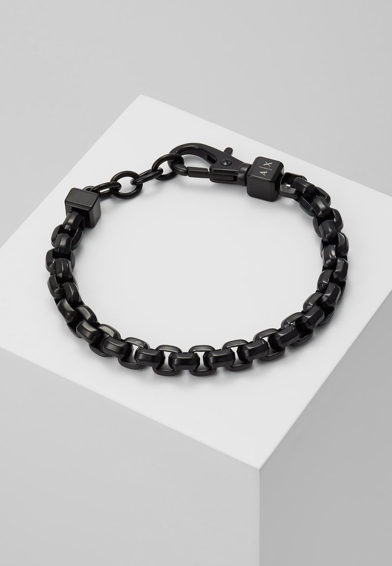 Bracelet en chaîne noire composé de maillons en métal brillant, avec des accents carrés et un fermoir. Surface lisse avec un design minimaliste.