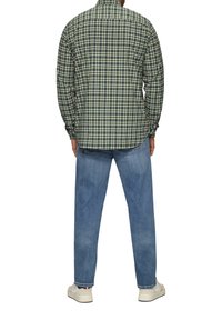 Koszula w kraty z długim rękawem w kolorach zielonym, granatowym i kremowym, z kołnierzykiem zapinanym na guziki. Połączona z jasnoniebieskimi dżinsami i białymi sneakersami.