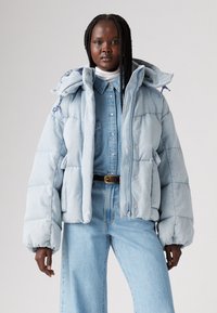 Light blue puffer jacket with a hood, featuring a quilted design, front snap buttons, and a slightly cropped fit, paired with matching denim.