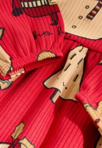 Roter gerippter Stoff mit einem festlichen Druck von Schneemännern und Stechpalme. Verfügt über einen elastischen Bund und kontrastierende beigefarbene Abschnitte mit Mustern.