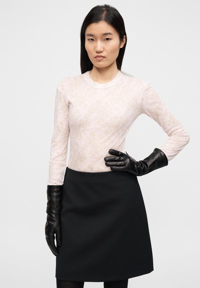 Haut à manches longues de couleur rose clair avec un motif floral, accompagné d'une jupe noire ajustée et de gants en cuir noirs. Texture lisse dans l'ensemble.