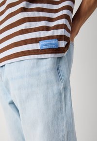 Brun og hvit stripete ribbet T-skjorte med blå etikett på kanten, kombinert med lyseblå slitte denimjeans.