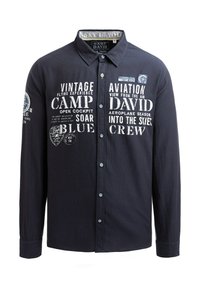 Dunkelblaue Knopfhülschen aus Stoff mit weißen gedruckten Texten und Grafiken, die mit der Luftfahrt in Verbindung stehen. Verfügt über einen Kragen und lange Ärmel.