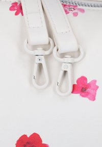 Witte leren tas met twee zilveren metalen clips, bloemenroze accenten en een zachte textuur. Ritsluiting aan de bovenkant.