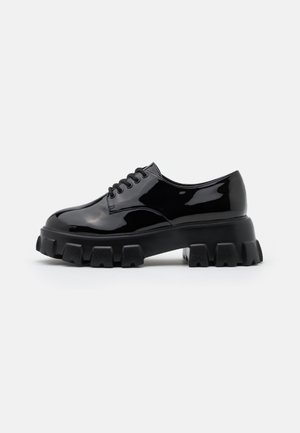 Zapatos de charol negro con suela gruesa, que presentan estrías texturizadas y cordones. La puntera redondeada y el diseño elegante ofrecen un aspecto contemporáneo.