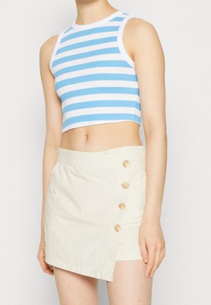 Kvinde iført en blå og hvidstribet ærmeløs crop top og en off-white asymmetrisk nederdel med fire knapper i siden og en lomme.