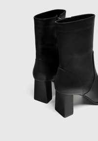 Bottines noires en cuir lisse avec un talon carré bloc, dotées d'une fermeture éclair et d'un détail de couture minimal.