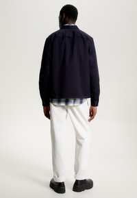 Marineblå skjorte med knapper og et ternet indlæg, parret med hvide bukser og sorte platformssko. Minimalistisk design og rene linjer.