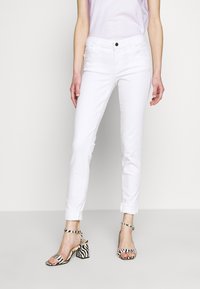Vaqueros de denim blanco con un corte ajustado, dobladillos acampanados y presillas para cinturón; combinados con sandalias de tacón de rayas en blanco y negro.