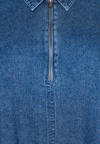 Farkkutakki, jossa on klassinen kaulus, näkyvä kullanvärinen vetoketju ja tummansininen kangas. Takissa on tekstuuri ja näkyvät ompelut.