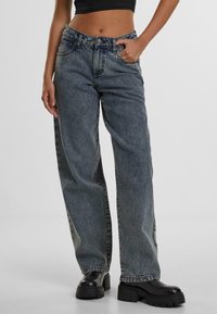 Lösa mörk denimjeans med blekta områden, femficksdesign och synlig sömnad. Bärs med kraftiga svarta platåstövlar.