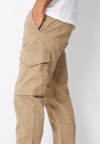 Beige cargobukser lavet af bomuld, med sidelommer, lige snit og minimale syningsdetaljer. Tekstureret stof med en mat finish.