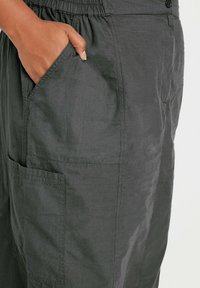 Harmaa cargo-housut, jotka on valmistettu kevyestä materiaalista, joissa on joustava vyötärö, sivutaskut ja minimaalinen ompelu.