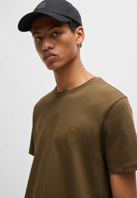 Olive green t-shirt with a round neckline and short sleeves. Features a small, textured black "BOSS" logo patch on the chest.
