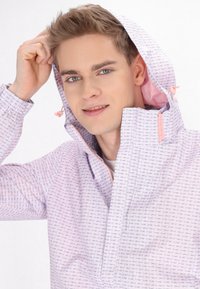 Giacca leggera con cappuccio realizzata in tessuto rosa pastello con motivo a pesci, tasche con zip e accenti rosa a contrasto.