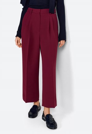 Pantaloni bordeaux a vita alta con pieghe, realizzati in un tessuto liscio. Abbinati a mocassini neri con un design texture.