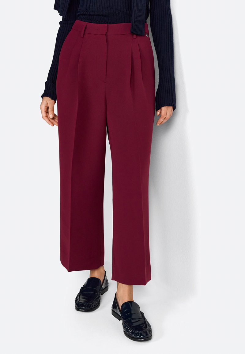 Pantalons taille haute bordeaux avec plis, en tissu lisse. Associés à des mocassins noirs, avec un design texturé.