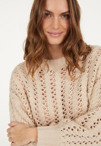 Hellbeige gestrickter Pullover mit lockerer Passform, offenem Muster und gerippten Bündchen, der ein strukturiertes und atmungsaktives Design präsentiert.