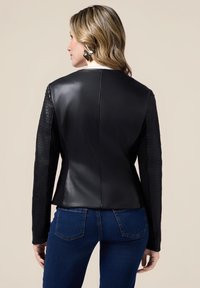 Sort læderjakke med strukturerede sorte ærmer, skræddersyet form og en glat ryg. Bærer den sammen med blå jeans, der viser en tætsiddende stil.