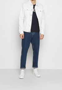 Bílá džínová bunda přes černé tričko, doplněná o srolované tmavě modré džíny a bílé tenisky. Jednoduchý design s kovovými knoflíky.