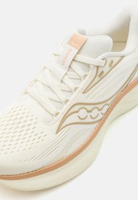 Baskets blanches de sport avec une tige en maille, des accents dorés, des panneaux latéraux texturés et une semelle rembourrée pour le confort.