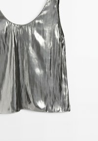 Metalická stříbrná tílko s kulatým výstřihem, které má hladký, reflexní povrch a volný, splývavý střih. Žádné viditelné švy.