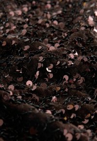 Black fabric covered in overlapping shiny pink sequins. The texture appears soft and layered, creating a dynamic surface effect.