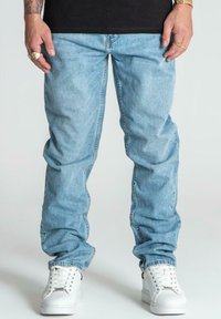 Jeans de mezclilla azul claro con un diseño de pierna recta, que cuentan con bolsillos laterales y cremallera, combinados con zapatillas blancas.